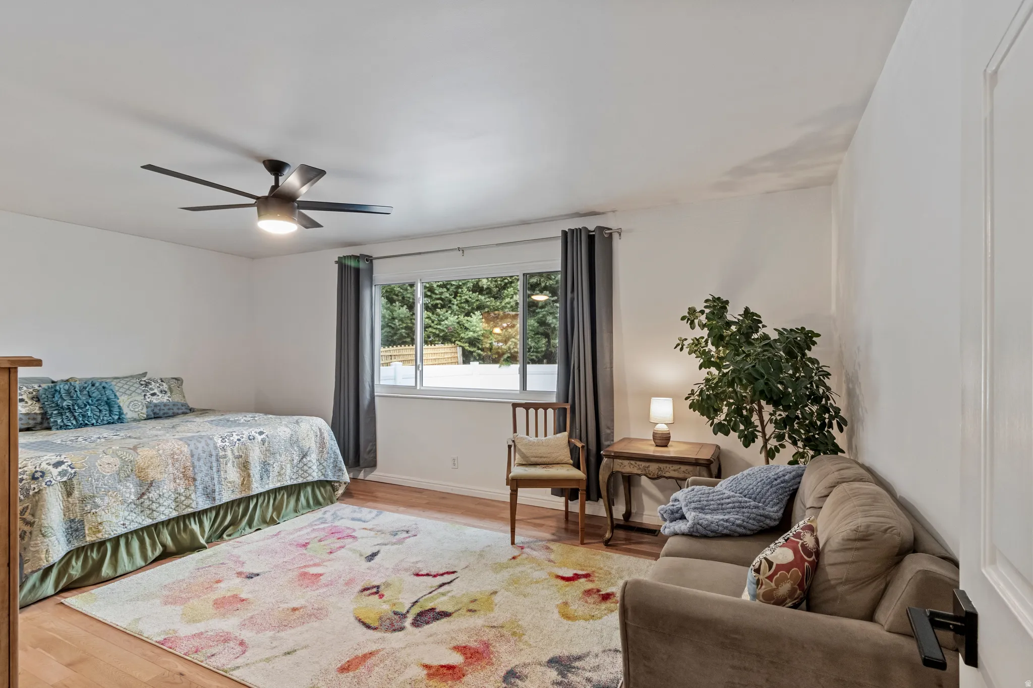 Spacious room featuring wood-finish flooring, a contemporary ceiling fan, and a large window with privacy curtains
