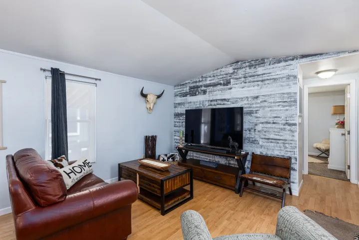 Living area featuring wood-finish flooring, a vaulted ceiling, and a prominent accent wall with a distressed wood-paneled finish