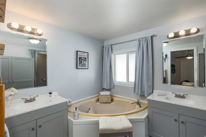 Bathroom featuring a corner built-in tub, two single vanities with undermount sinks, and a window with privacy glass