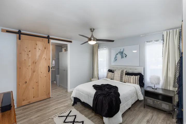 Spacious room featuring wood-finish flooring, a ceiling fan, and two windows with white curtains
