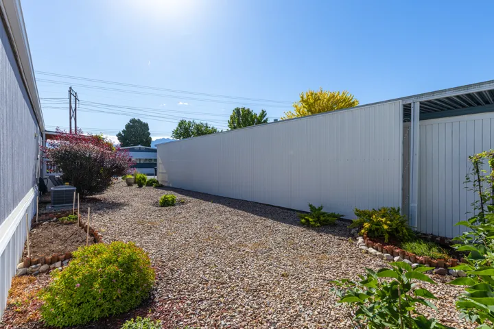 Gravel-covered outdoor space featuring various plantings and a white corrugated metal fence