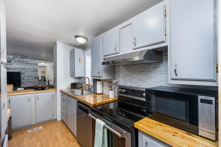 Kitchen featuring light gray cabinetry with brushed nickel pulls, wood-finish countertops, stainless steel appliances, a mosaic tile backsplash, and wood-finish flooring