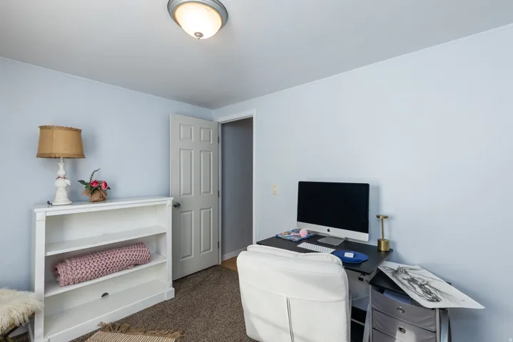 Light blue walls and textured carpeting define this room, featuring a built-in flush-mount ceiling light fixture, a paneled interior door, and white baseboards