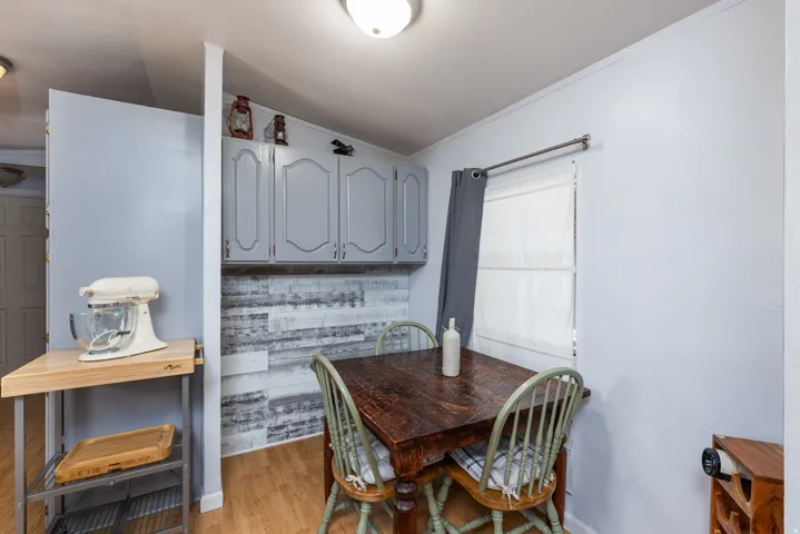 Dining area featuring a dark wood-finish table, light wood-finish flooring, and a window with a sheer white blind