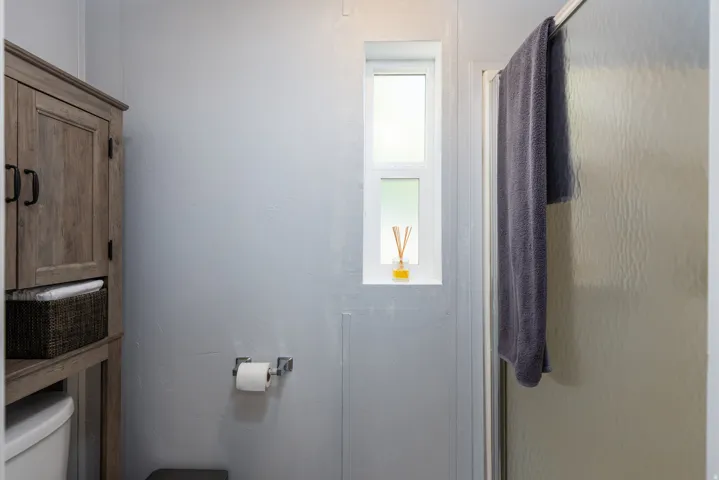 Bathroom featuring an enclosed shower with frosted glass, a vertical window, and a wood-finish storage cabinet
