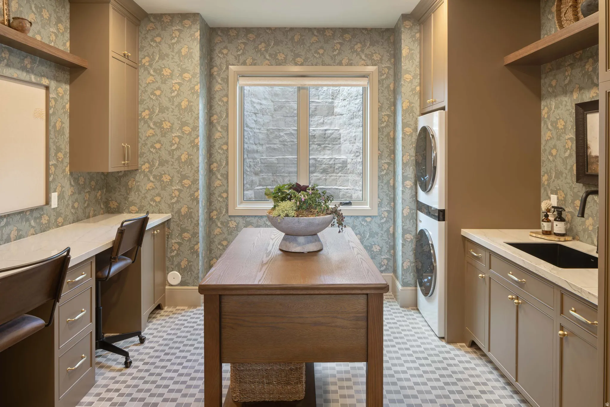 Dedicated laundry room featuring a stacked washer and dryer, a black basin sink with a wall-mounted faucet, and custom cabinetry with gold hardware