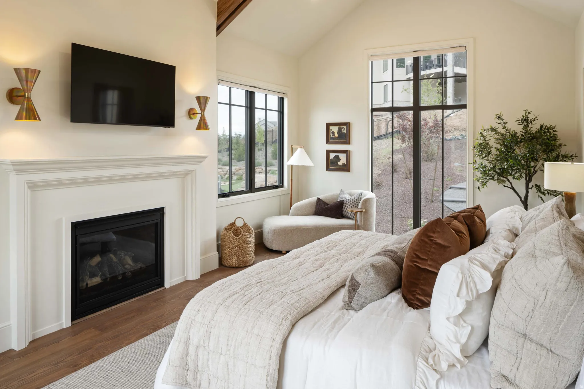 Vaulted ceiling room featuring a decorative fireplace with a classic mantel, wood-finish flooring, and large black-framed windows