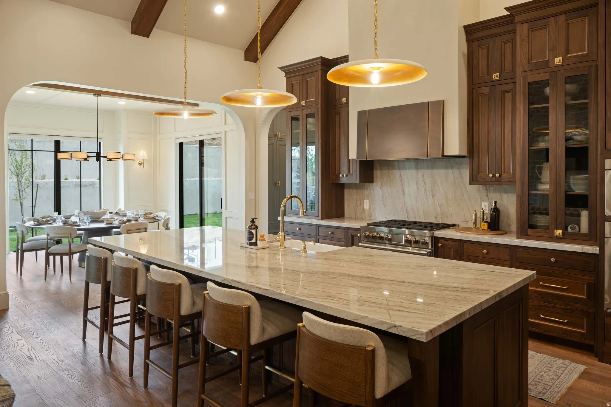 Spacious kitchen featuring a large central island with a stone countertop, custom dark wood cabinetry, stainless steel range with matching hood, and wood-finish flooring
