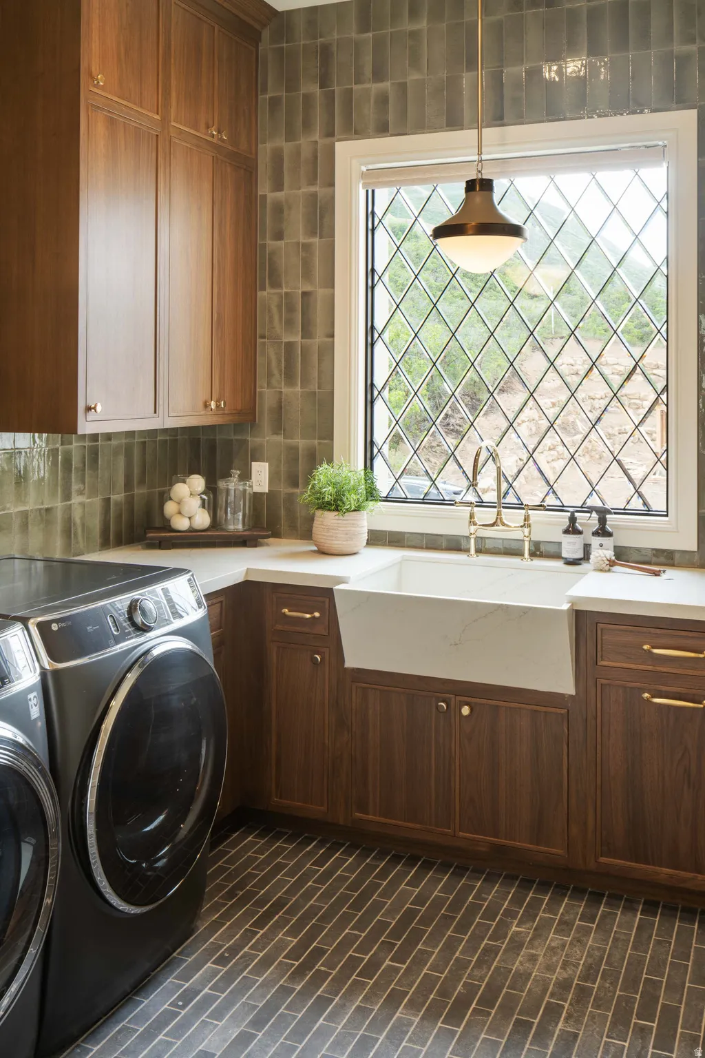 Laundry room featuring wood-finish cabinetry, dark rectangular floor tiling, and a white farmhouse sink with a brass faucet