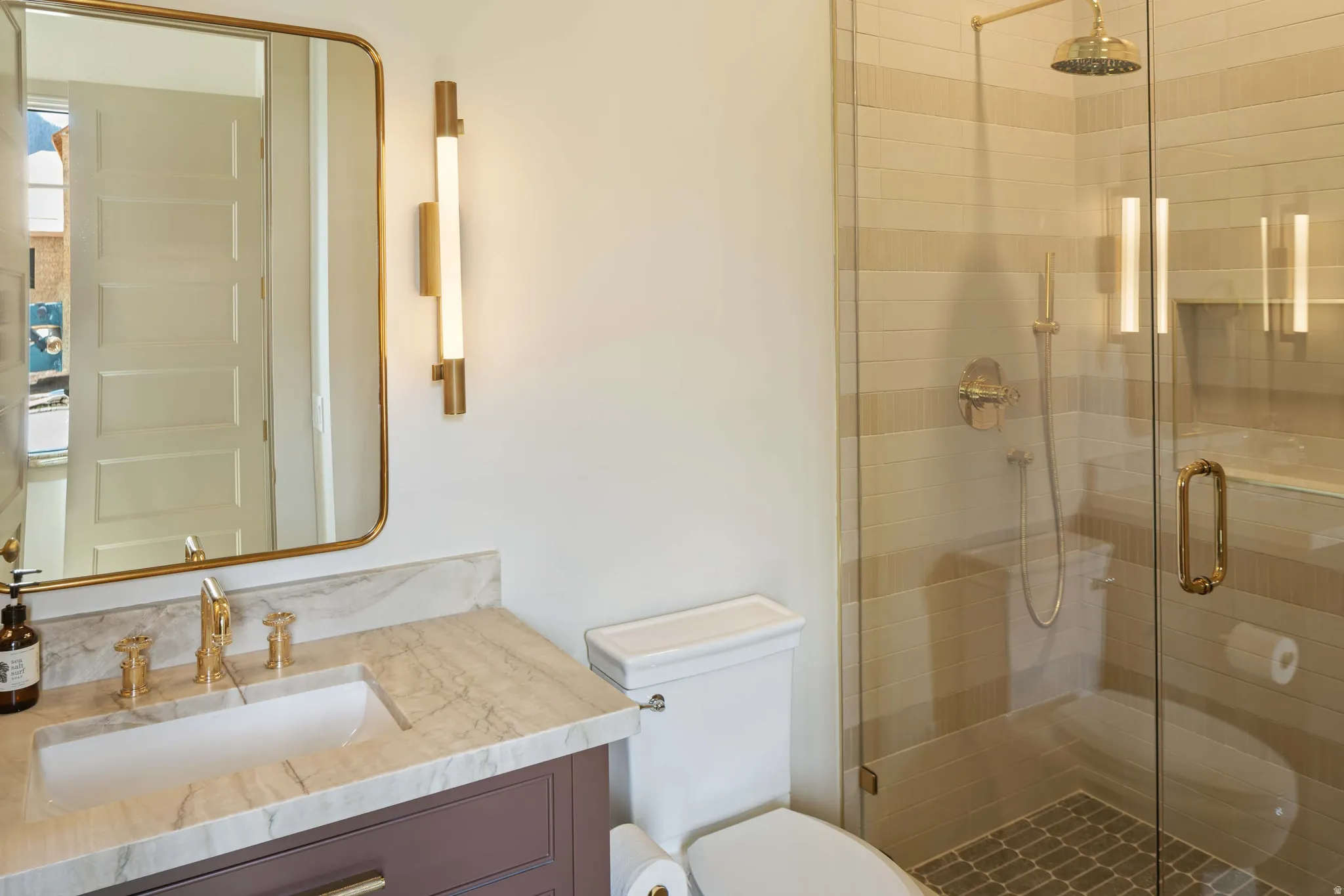 Bathroom featuring a glass-enclosed shower with a rainfall showerhead, a vanity with a stone countertop and integrated sink, and gold-finish fixtures