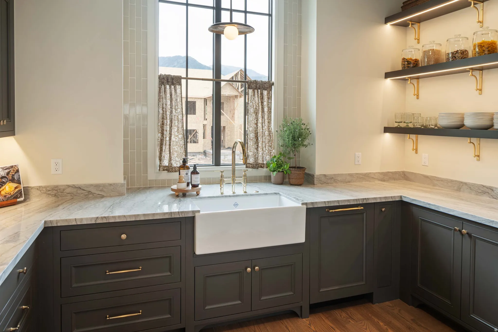 Kitchen featuring a white apron-front sink with a gold-tone faucet, dark cabinetry with gold-tone hardware, and light-colored countertops