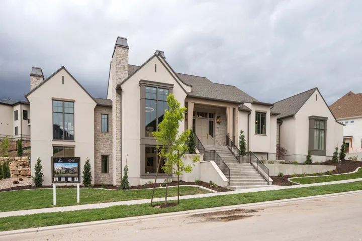 Stately exterior featuring stucco and stone finishes, prominent gabled roofs, a grand entry staircase with wrought iron railings, large picture windows, and integrated landscaping with mature trees
