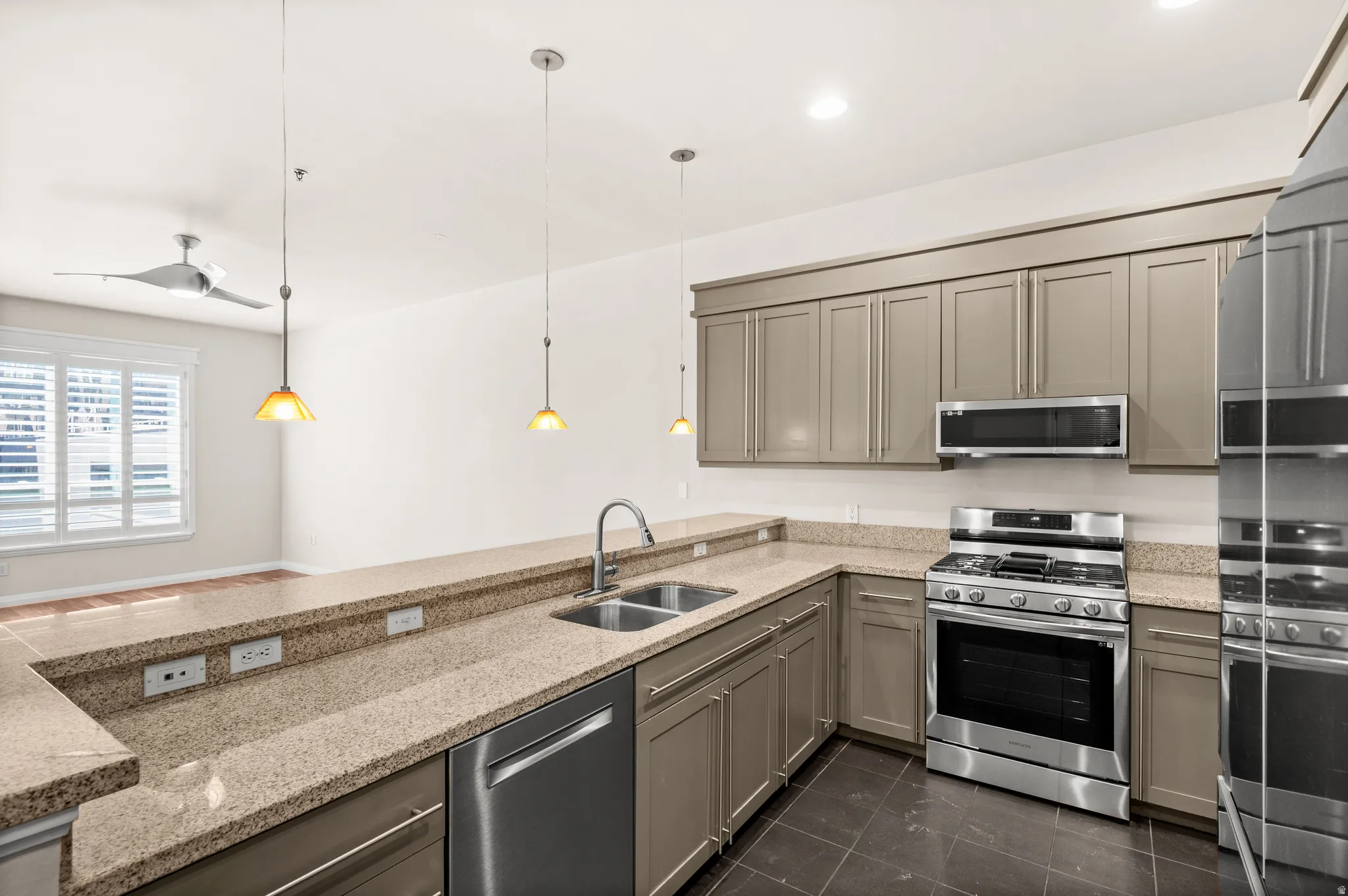 Kitchen featuring granite countertops, stainless steel appliances including a gas range and microwave, dual basin sink with a high-arc faucet, and pendant lighting