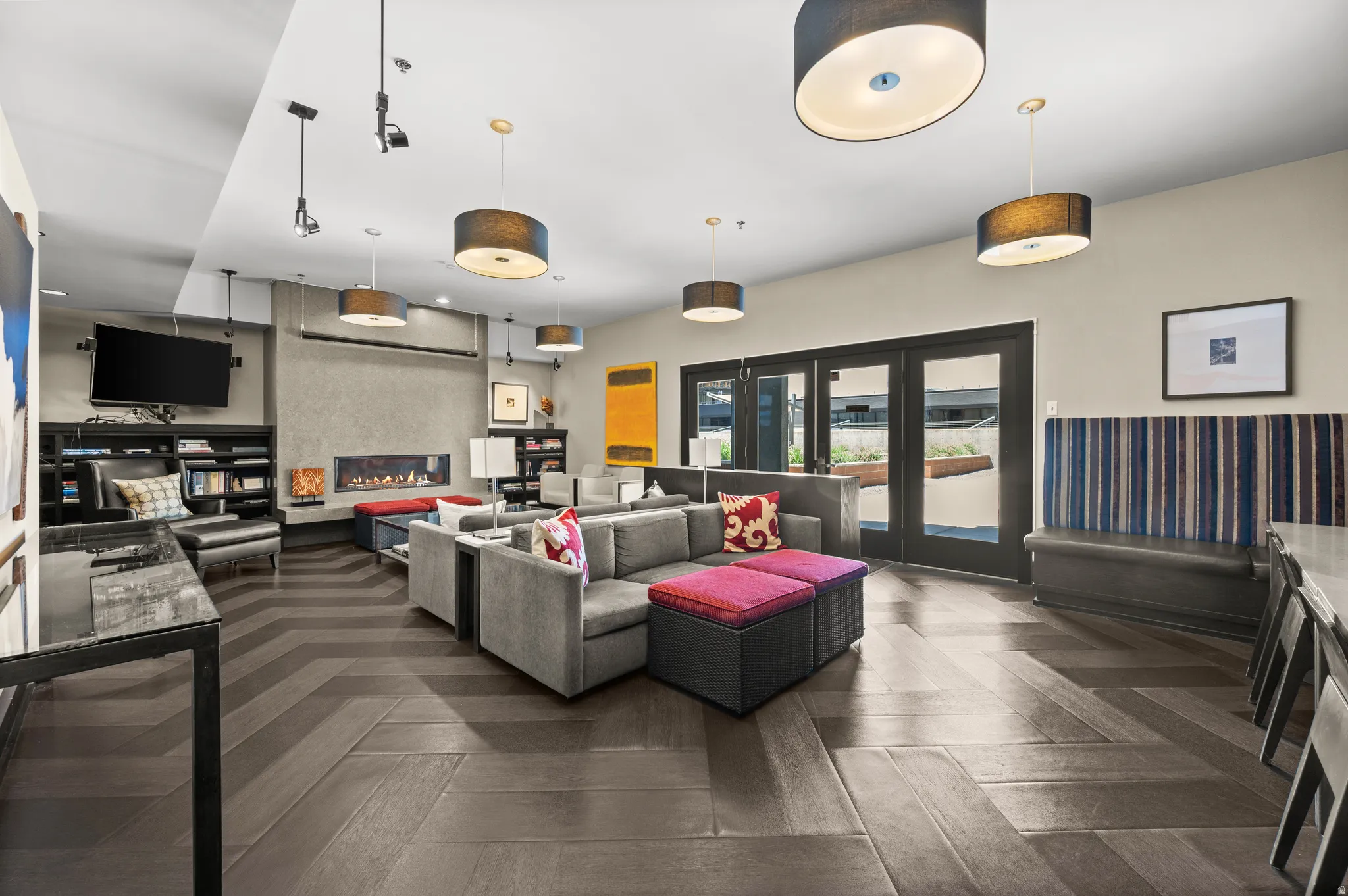 Spacious gathering room featuring wood-finish flooring with a herringbone pattern, a built-in linear fireplace, and multiple drum pendant lights