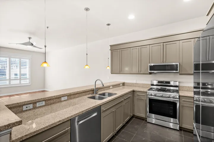 Kitchen featuring granite countertops, stainless steel appliances including a gas range and microwave, dual basin sink with a high-arc faucet, and pendant lighting