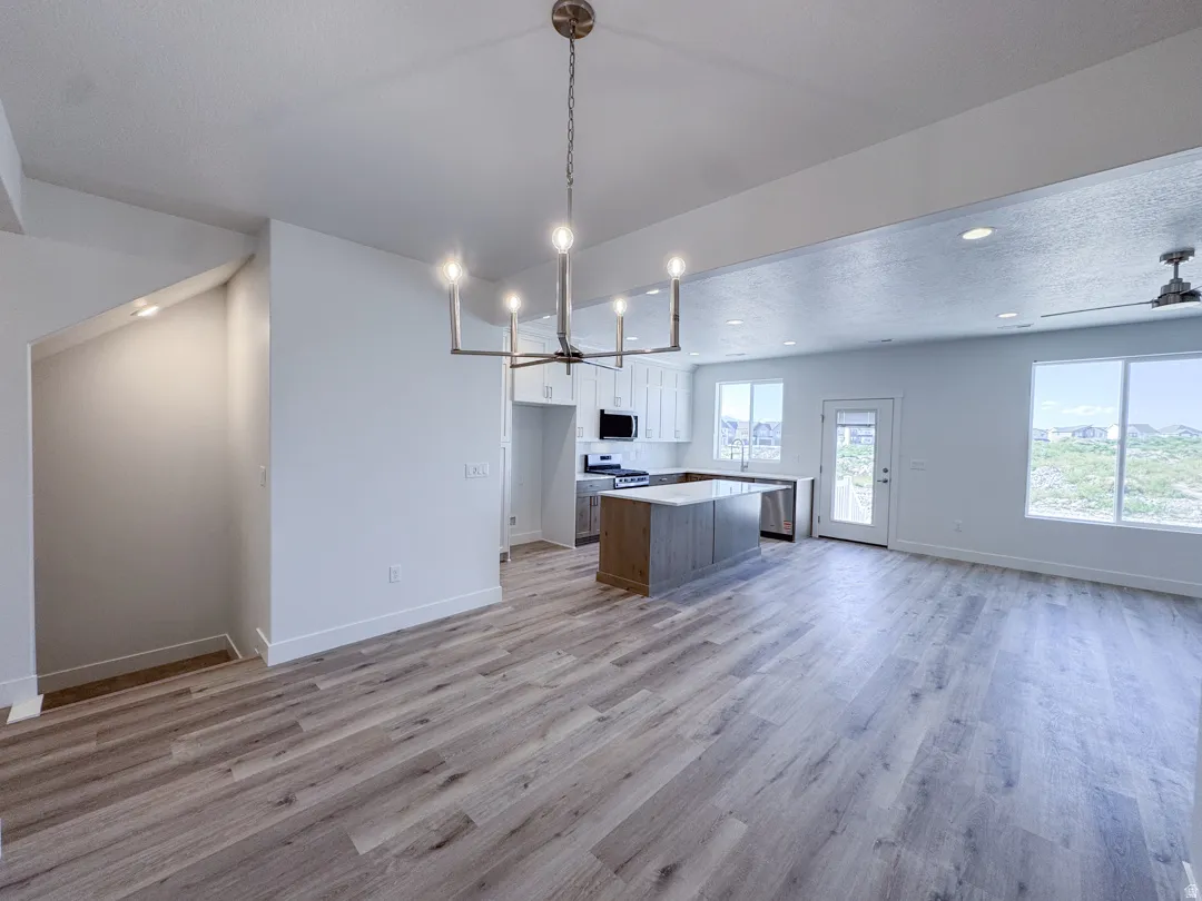 Open-concept living space featuring wood-finish flooring, a modern kitchen with a large island, white cabinetry, and stainless steel appliances