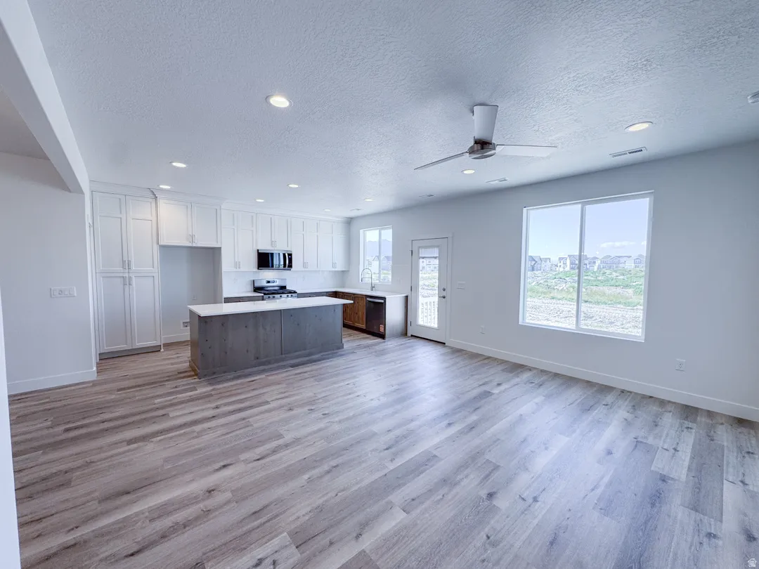 Open-concept living space featuring wood-finish flooring, a contemporary kitchen with white cabinetry and a central island, recessed lighting, and a ceiling fan
