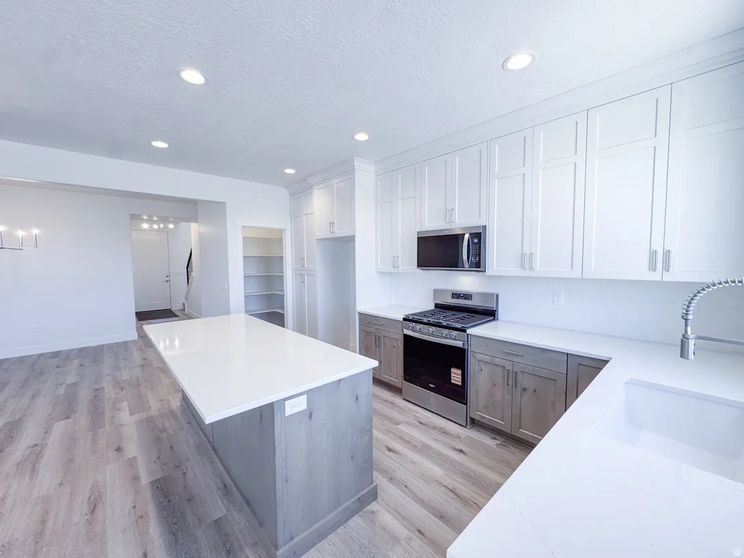 Modern kitchen featuring a large center island, white shaker cabinetry, stainless steel appliances, and wood-finish flooring