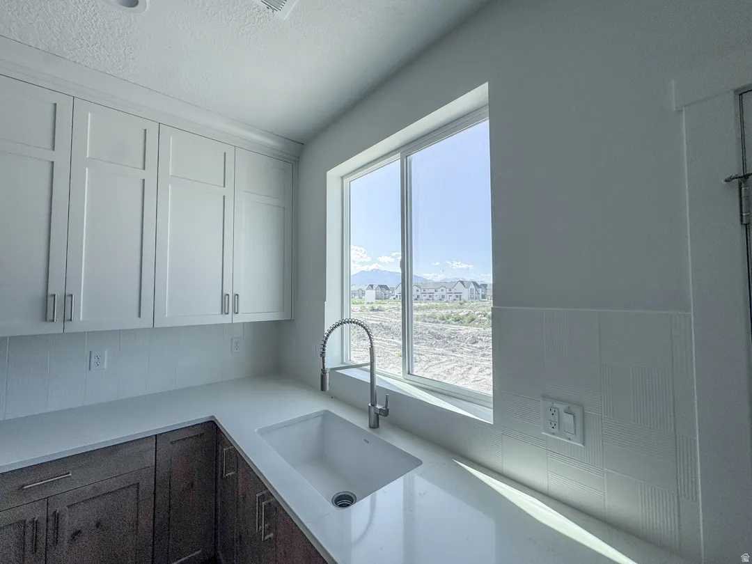 Kitchen featuring white shaker-style upper cabinetry with brushed nickel hardware, lower wood-finish cabinetry, a white countertop with an integrated sink, and a gooseneck pull-down faucet