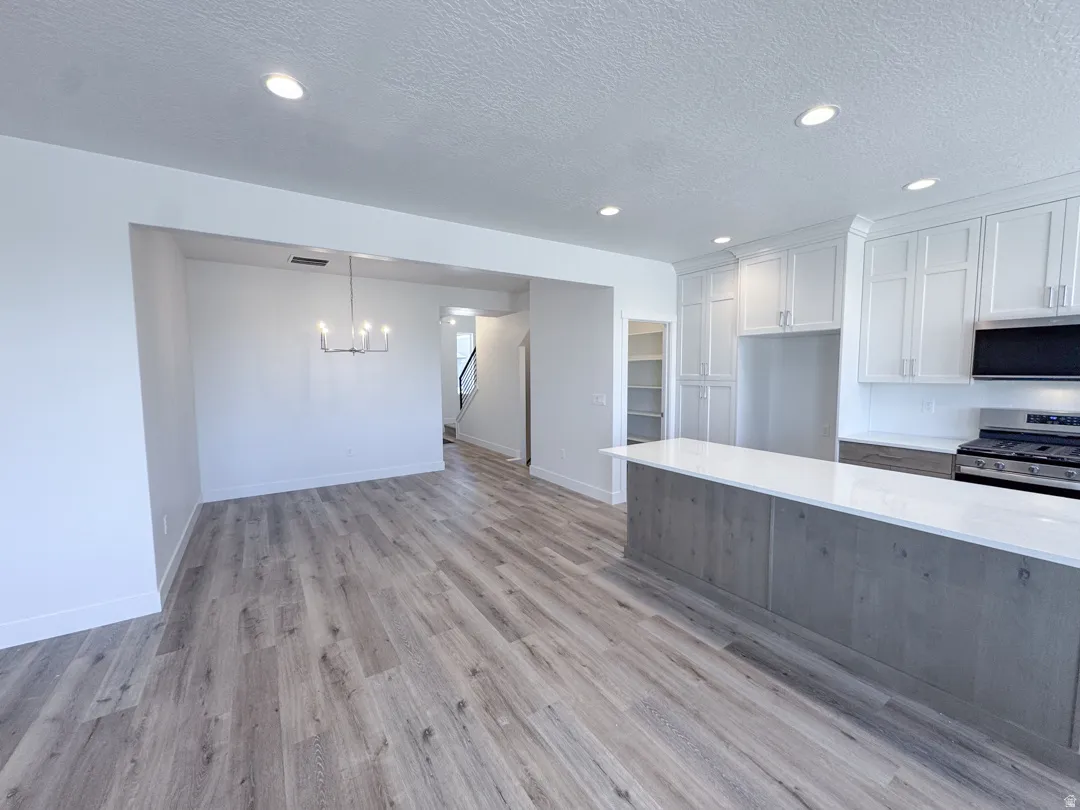 Open-concept kitchen and dining area featuring wood-finish flooring, white shaker-style cabinetry, and a spacious island with a light-toned countertop