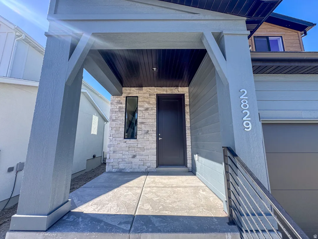 Modern entry featuring a prominent gray porch column, stone veneer accent wall, sleek dark entry door, and a vertically oriented window