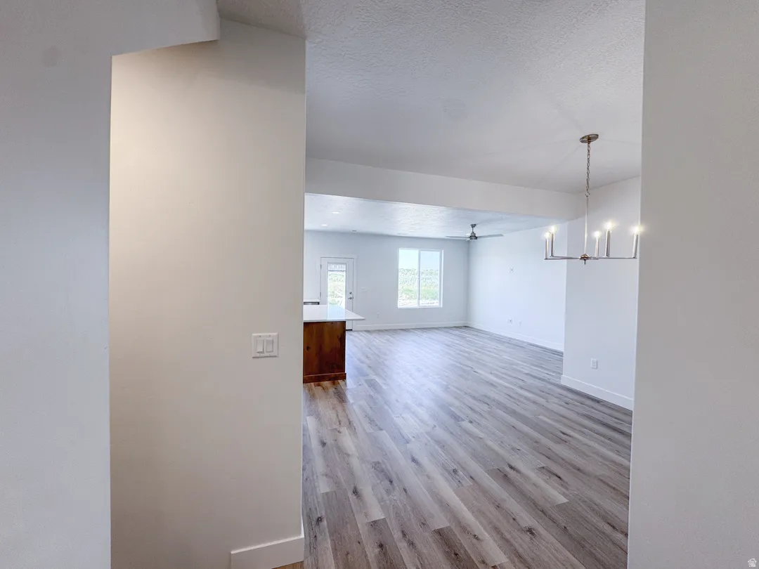 Spacious interior featuring wood-finish flooring, a contemporary chandelier, and a ceiling fan