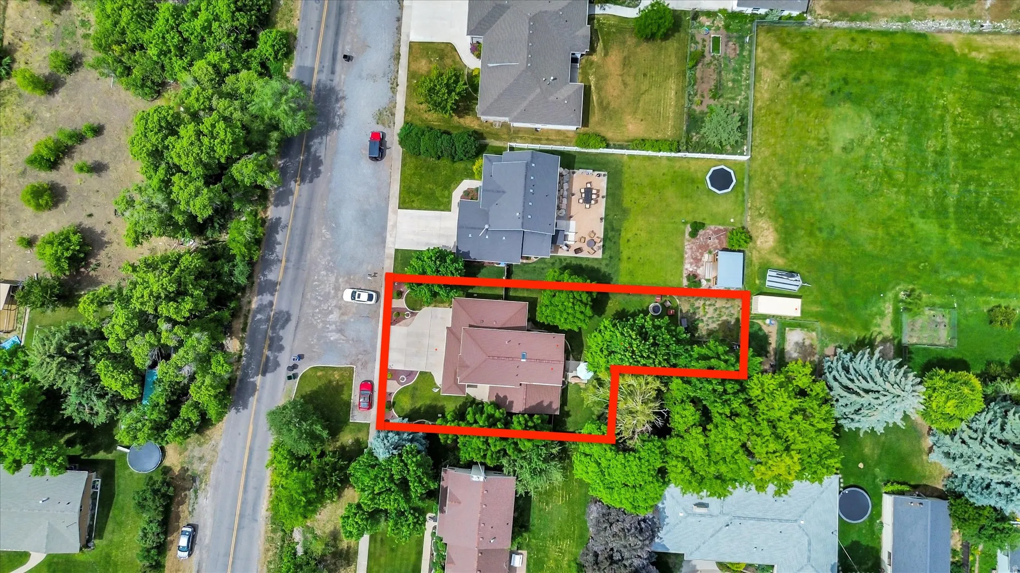 Aerial property perspective showcasing the residential structure, surrounding mature trees, a defined parcel boundary, and a paved driveway