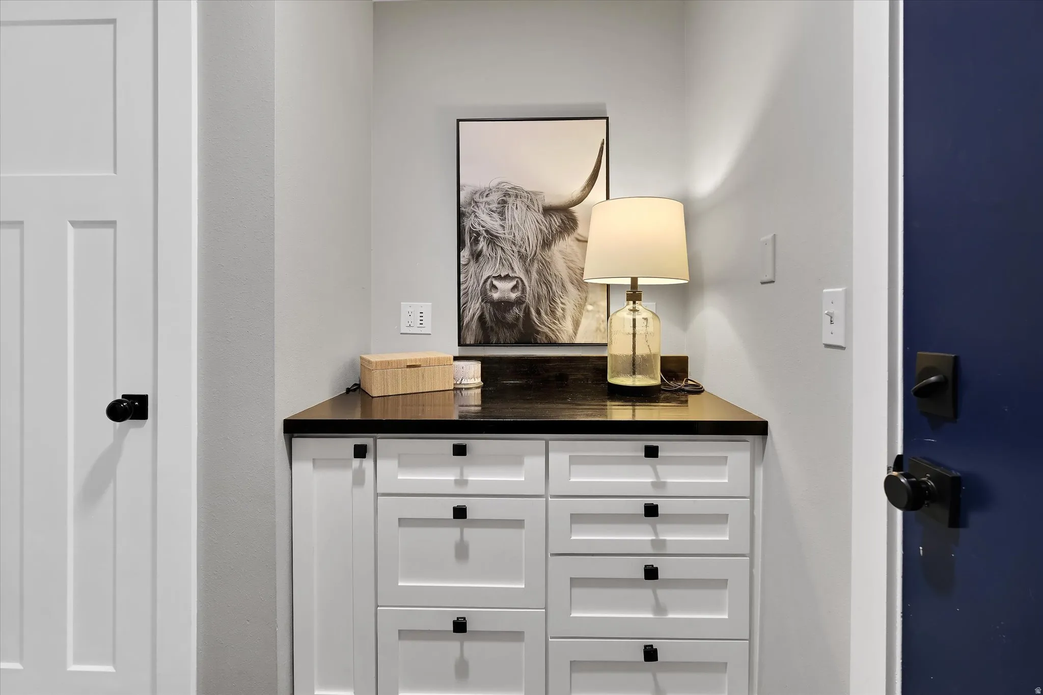 Built-in white cabinetry featuring multiple drawers with matte black hardware, dark countertop, and light gray wall paint