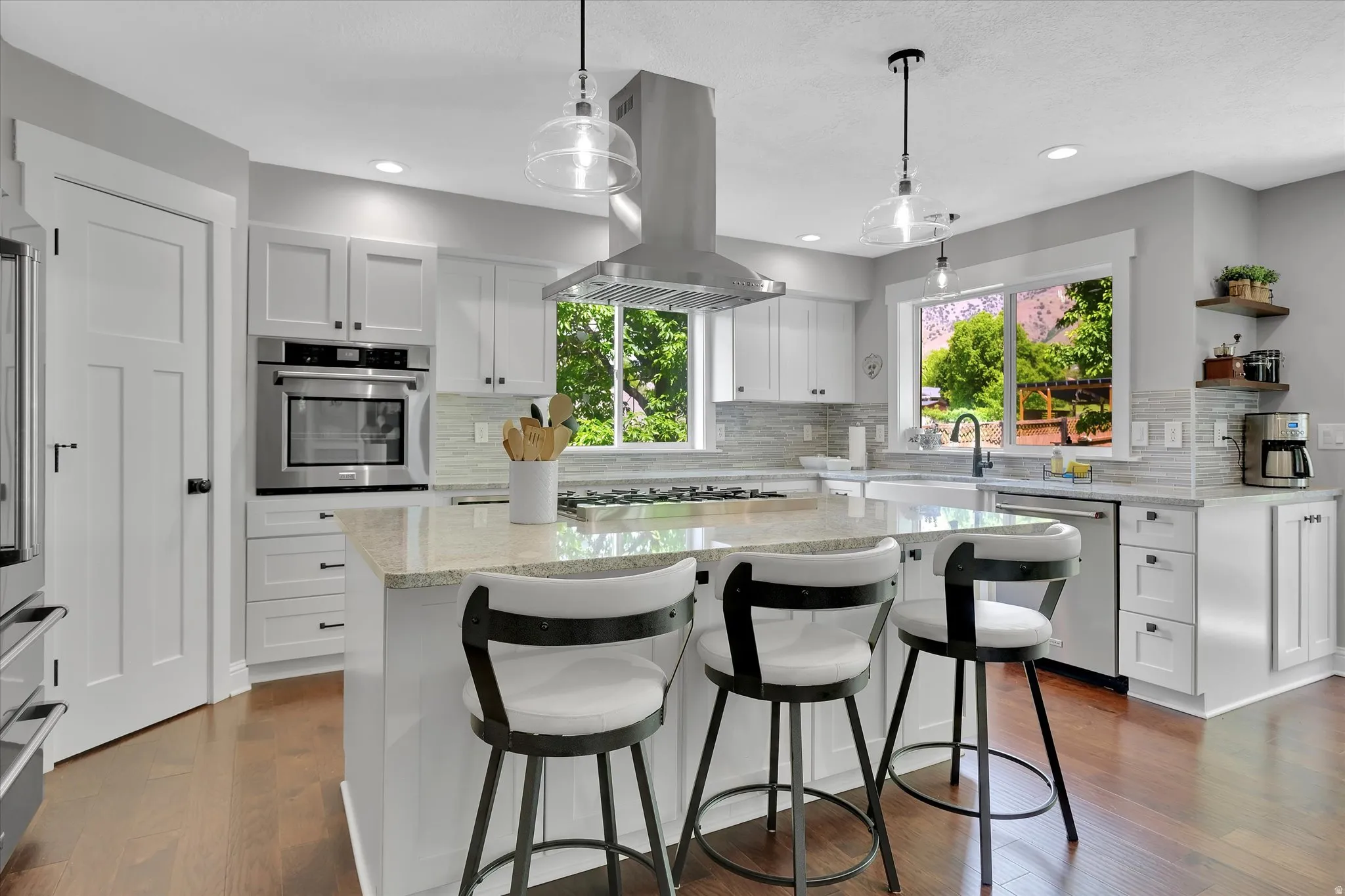 Contemporary kitchen featuring white cabinetry, a central island with a stone countertop, stainless steel appliances, and wood-finish flooring