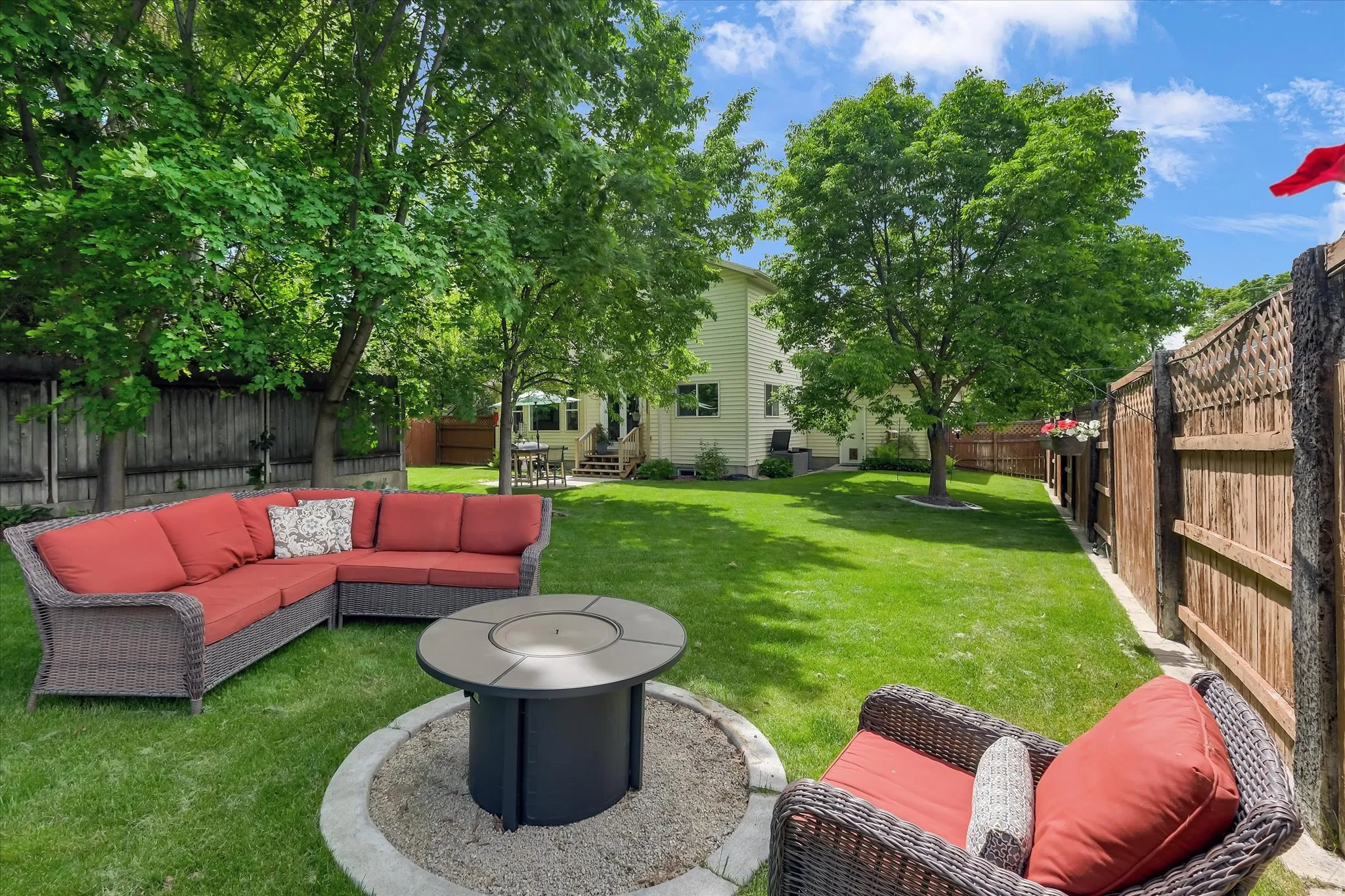 Spacious backyard featuring a manicured lawn, established shade trees, wood privacy fencing, and a built-in fire pit with stone surround