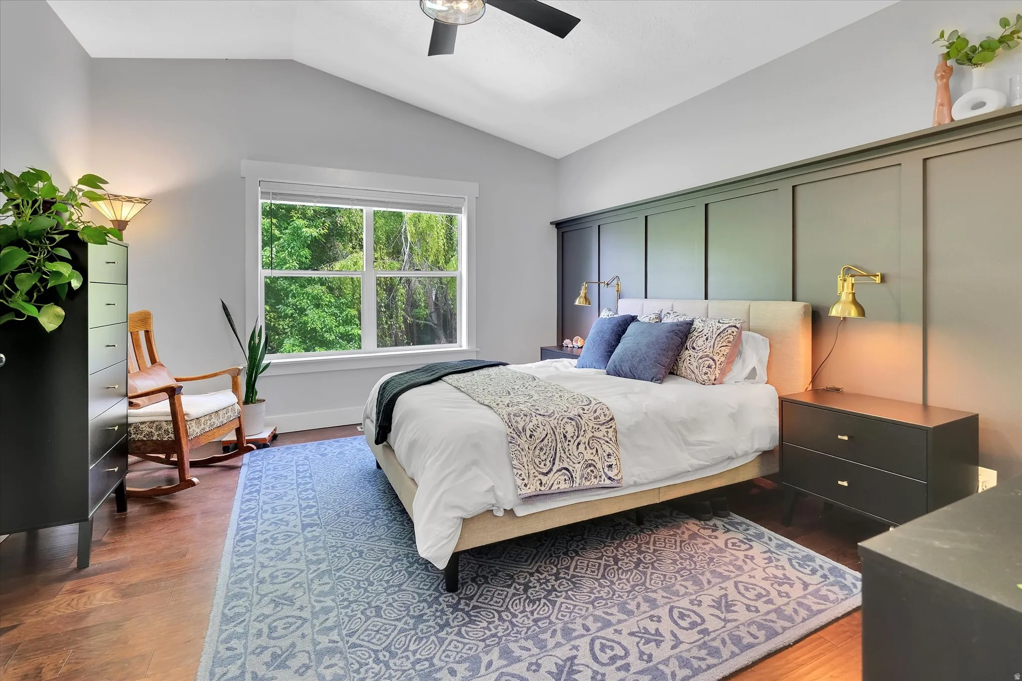 Vaulted ceiling bedroom featuring wood-finish flooring and a decorative accent wall with integrated shelving
