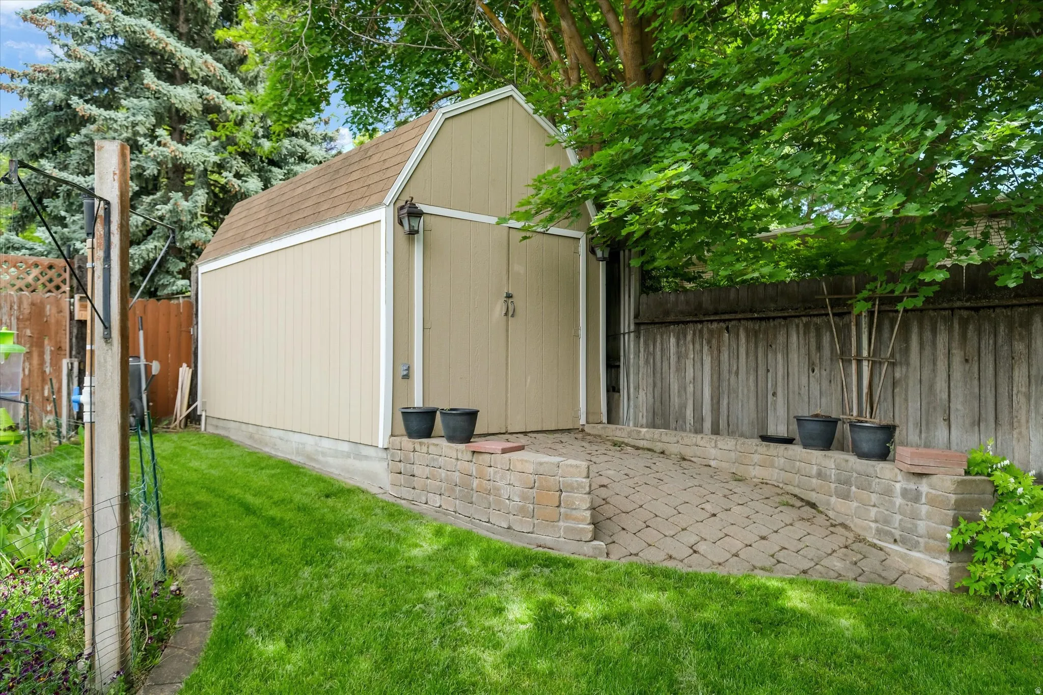 Expansive backyard featuring a gambrel-roofed storage shed with double doors, exterior lighting fixtures, and a paved ramp for access