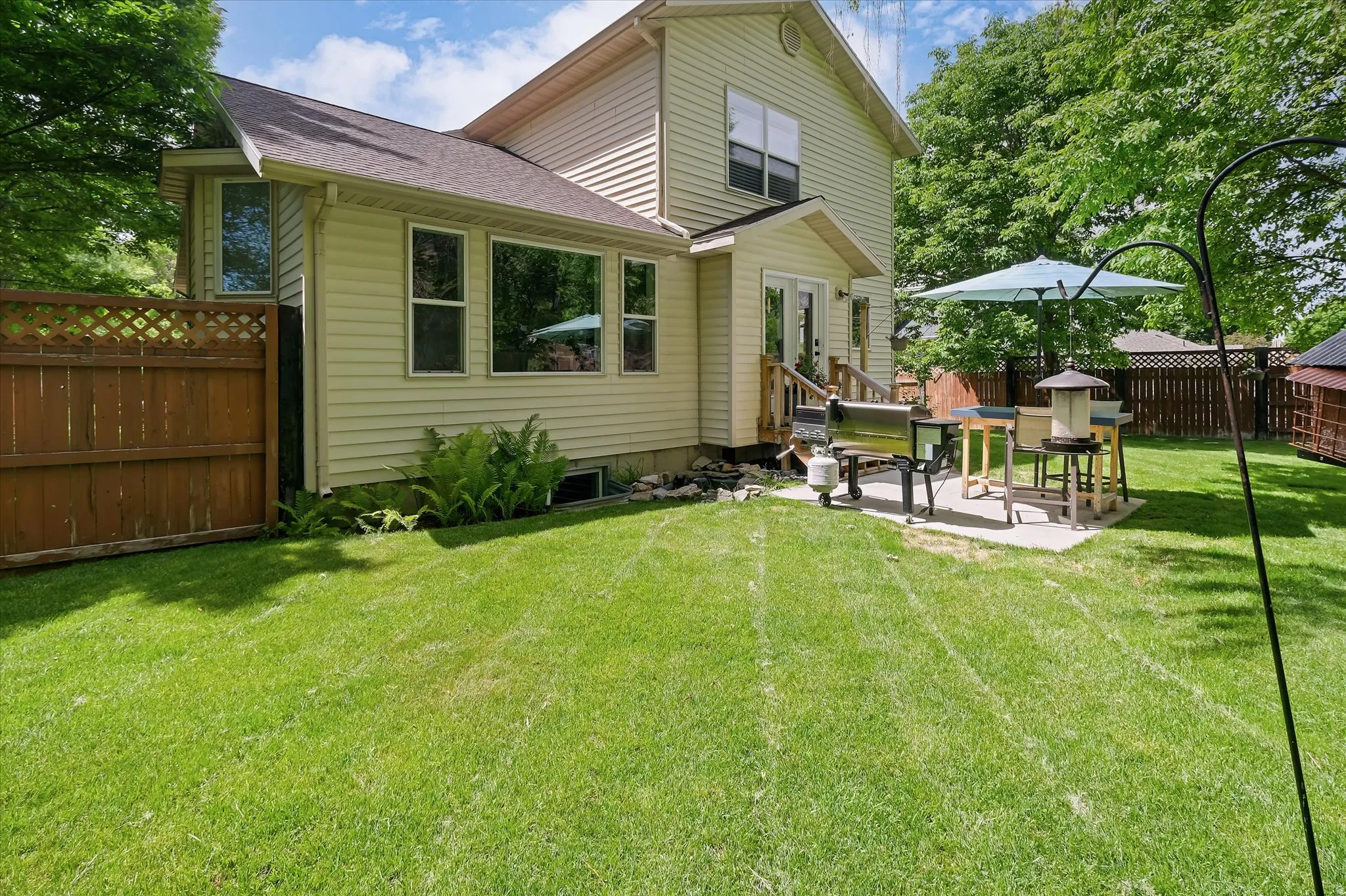 Expansive backyard featuring a lush lawn, privacy fencing, and a concrete patio