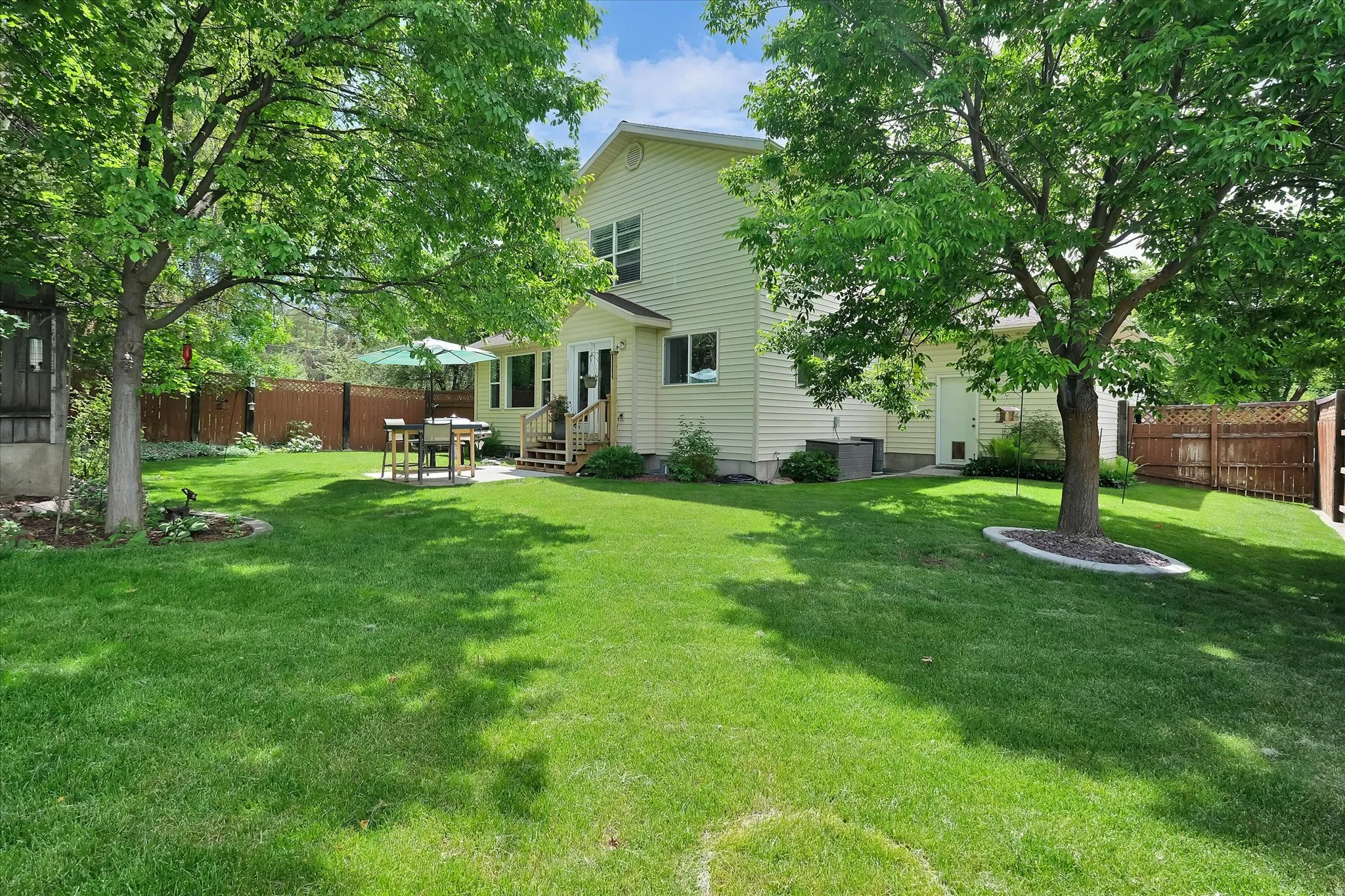 Expansive green lawn featuring mature shade trees, a rear patio, and a privacy fence