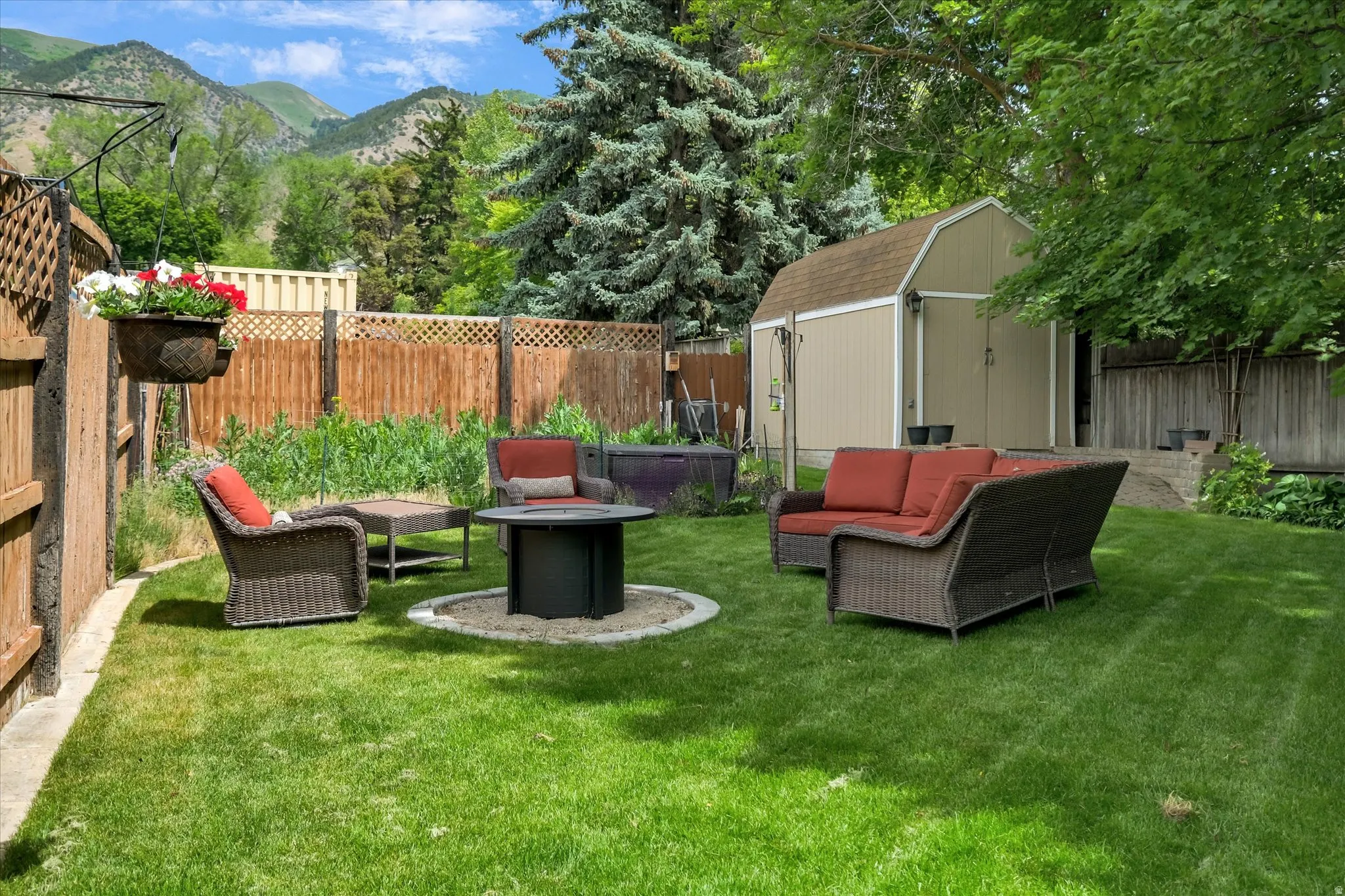 Expansive fenced backyard featuring a manicured lawn, a fire pit area with gravel surround, and a tan storage shed with a brown roof