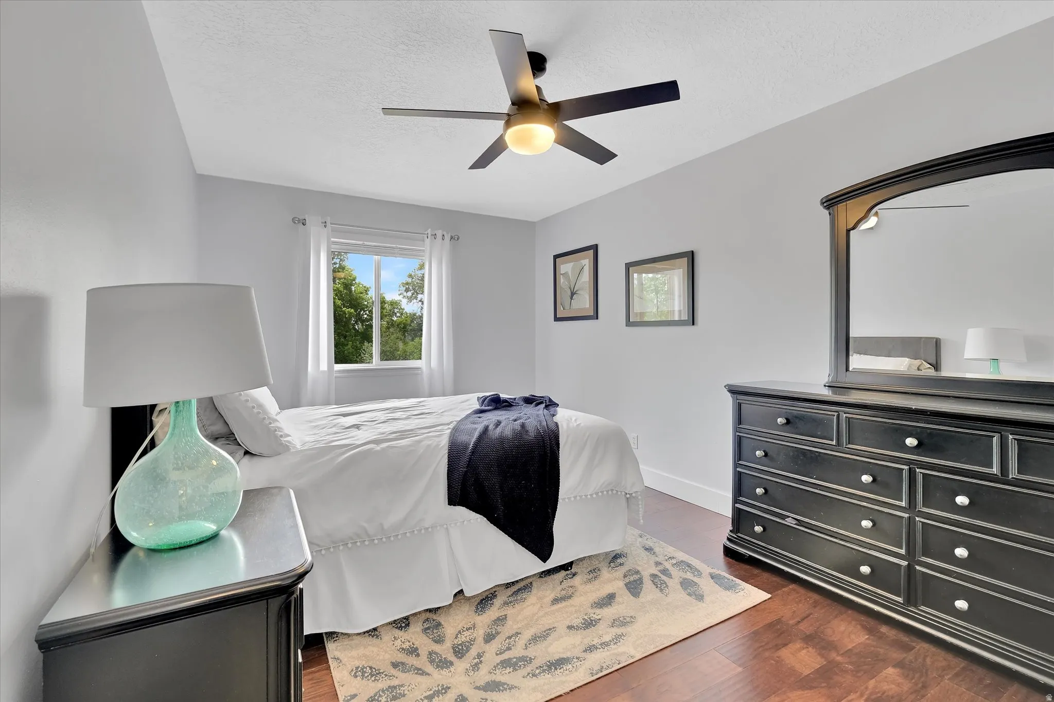 Bright interior space featuring a window with exterior scenery, dark wood-finish flooring, a ceiling fan with integrated lighting, and light-colored walls with white trim