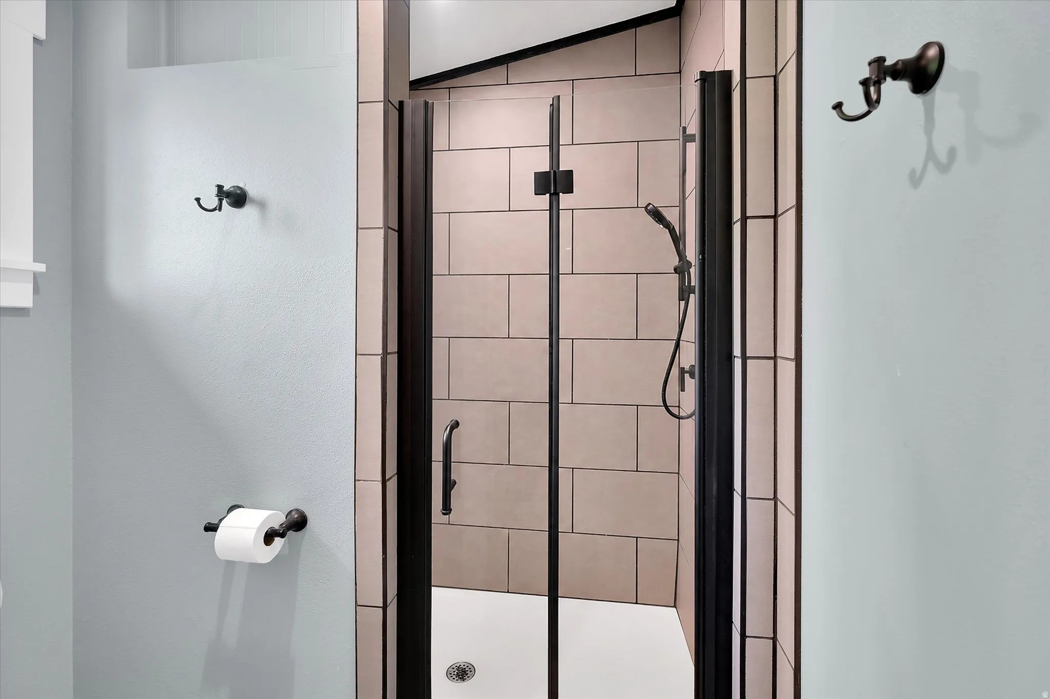 Shower enclosure featuring subway tile surround, matte black shower fixtures, clear glass door, and white shower pan