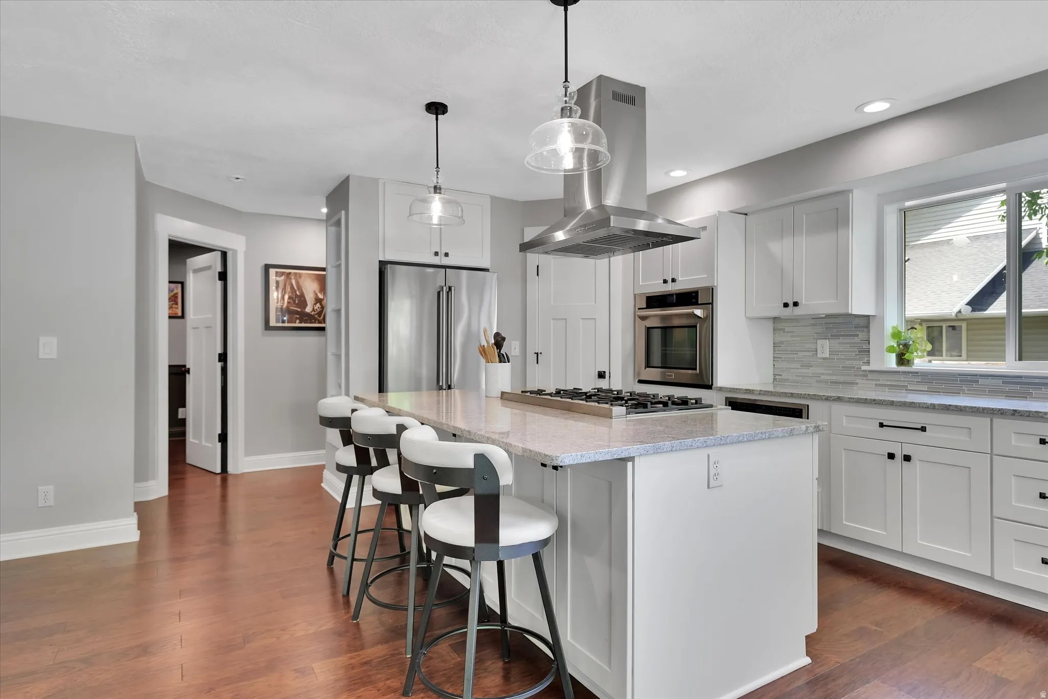 Gourmet kitchen featuring a large island with integrated gas cooktop, stainless steel oven, white shaker cabinetry, and wood-finish flooring