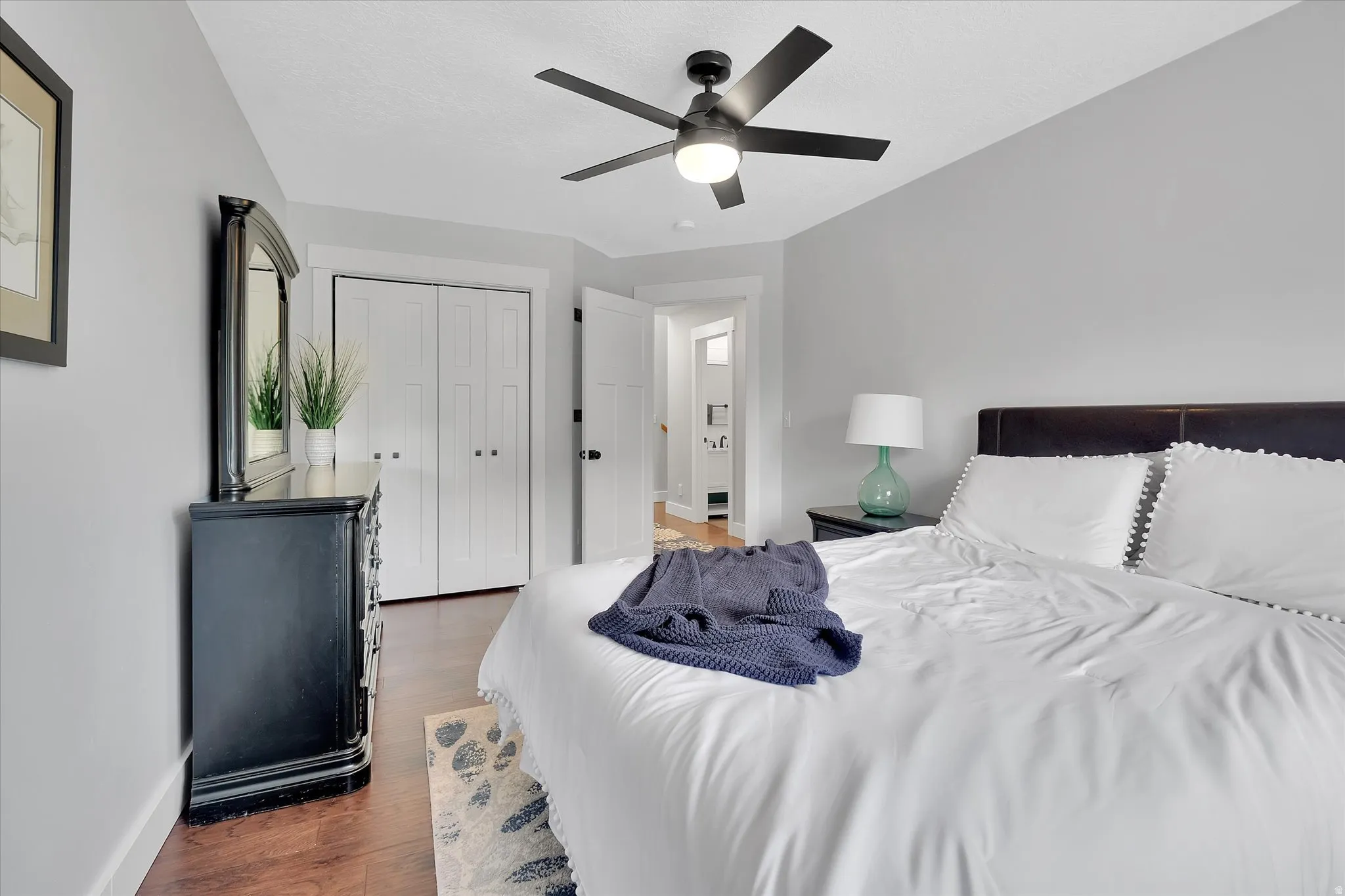 Spacious bedroom featuring wood-finish flooring, a contemporary ceiling fan with integrated lighting, and light gray wall finishes