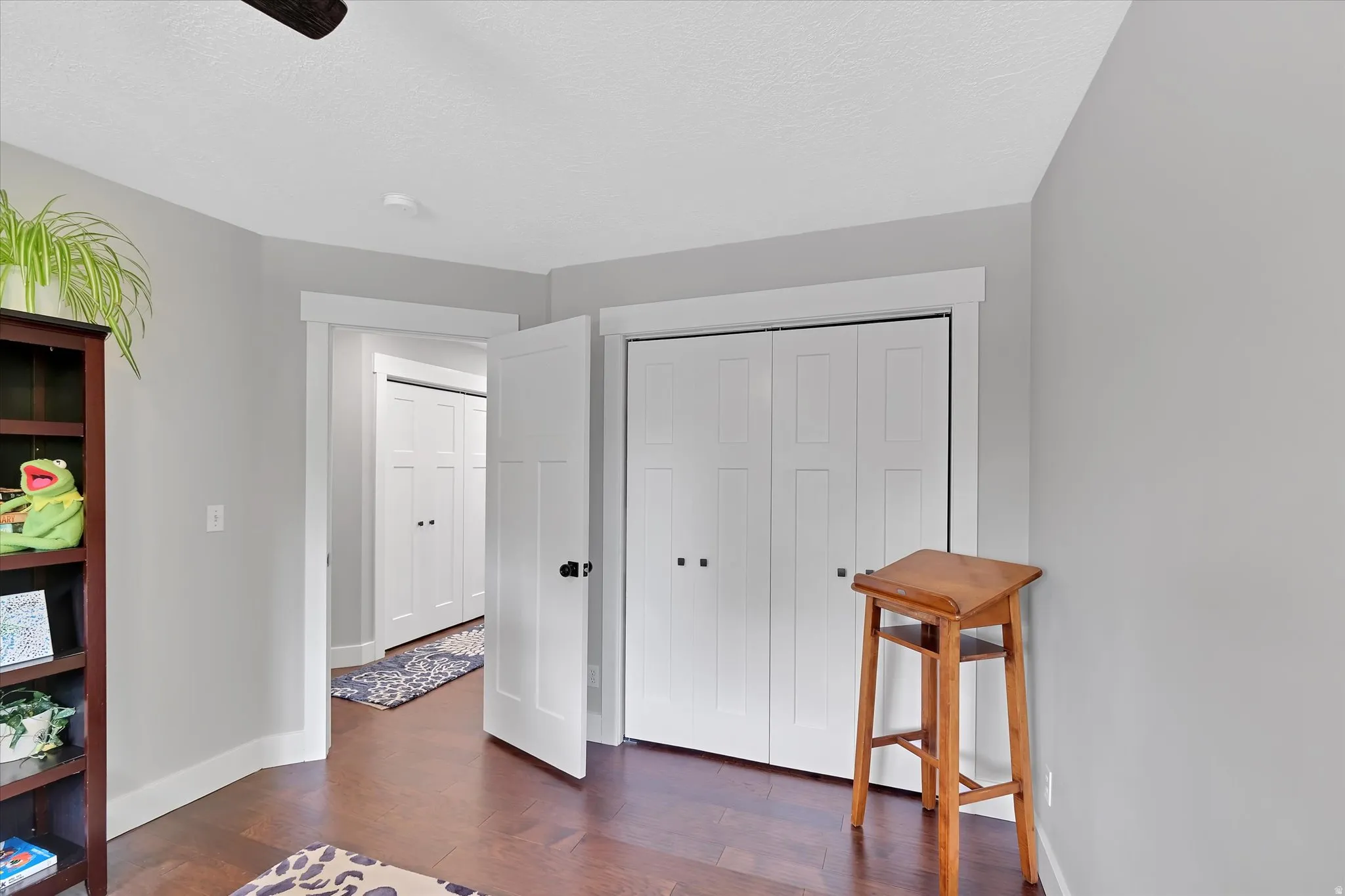 Room featuring wood-finish flooring, light gray walls, white trim, and white bi-fold closet doors with black hardware