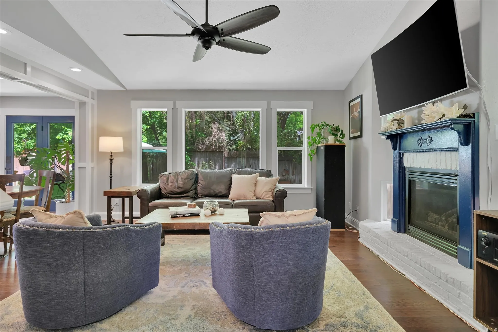 Living area featuring hardwood flooring, a fireplace with a blue mantel and white brick hearth, and a ceiling fan