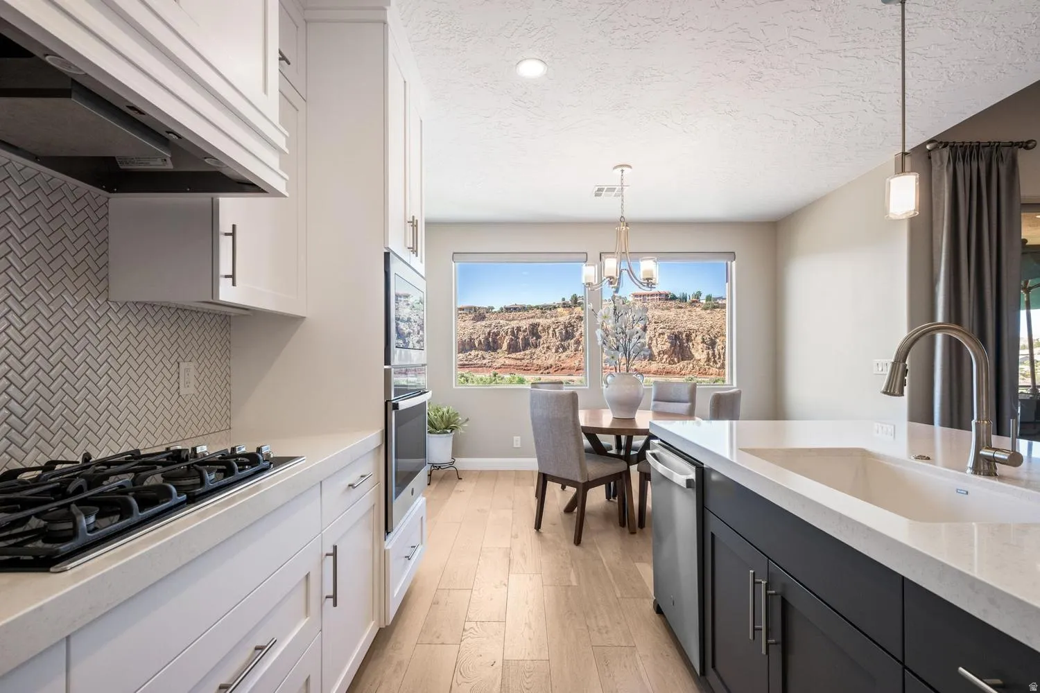 Modern kitchen featuring light cabinetry, herringbone tile backsplash, built-in ovens, gas cooktop, and a peninsula with an undermount sink
