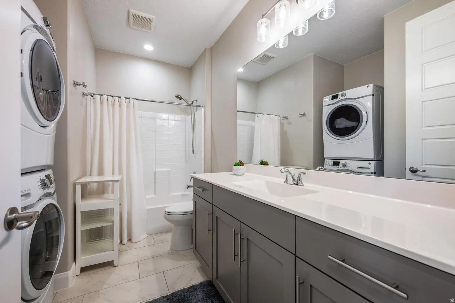 Well-appointed bathroom featuring a spacious vanity with a white countertop and gray cabinetry, a full-width mirror, and a modern light fixture