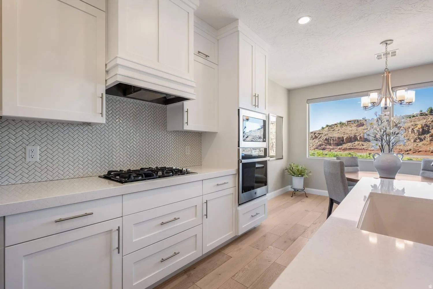 Modern kitchen featuring a gas range cooktop, chevron tile backsplash, white shaker cabinetry, stainless steel double wall oven, and wood-finish flooring