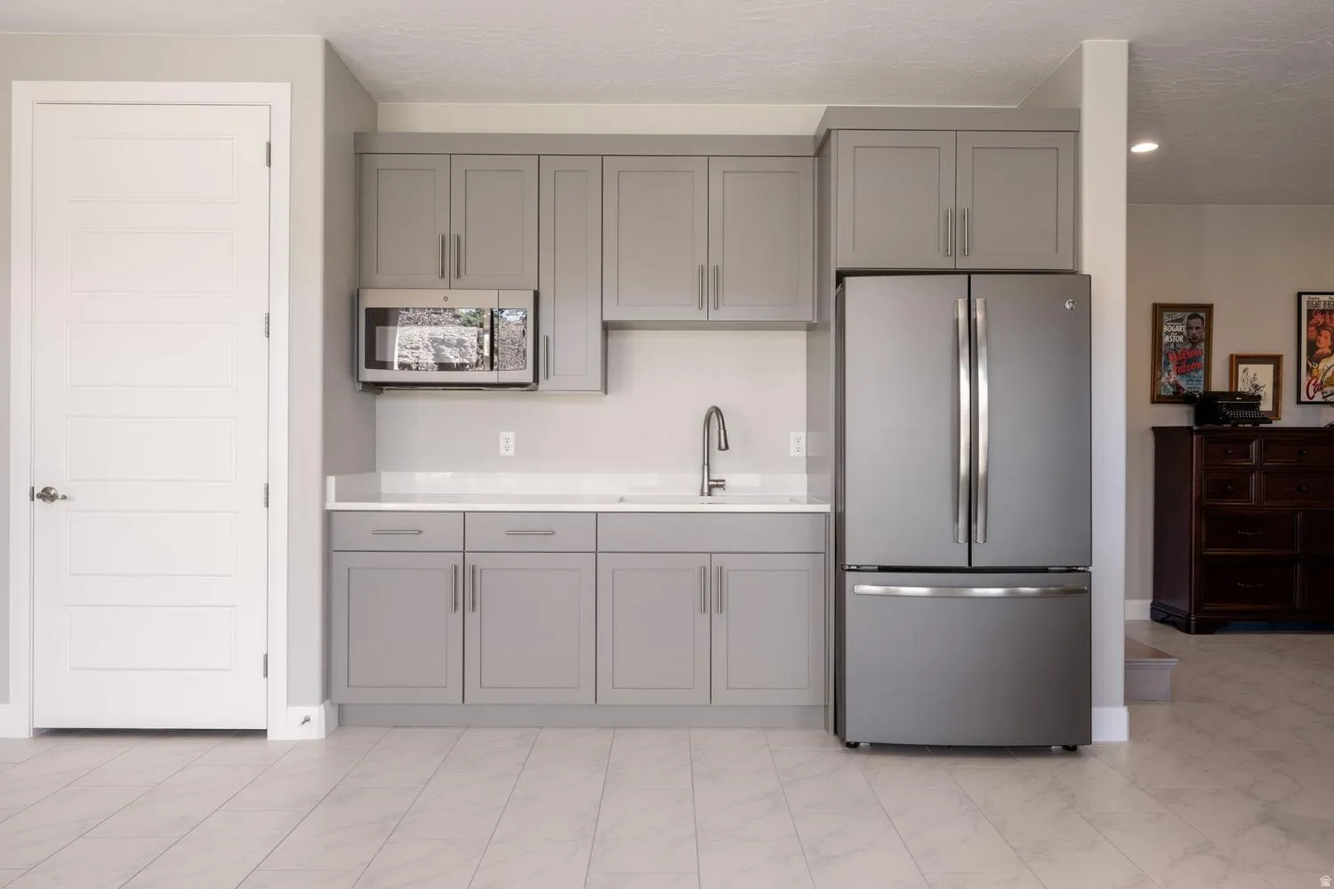 Compact kitchen area featuring gray cabinetry, stainless steel appliances, a sink with a gooseneck faucet, light-toned countertops, and wood-finish flooring