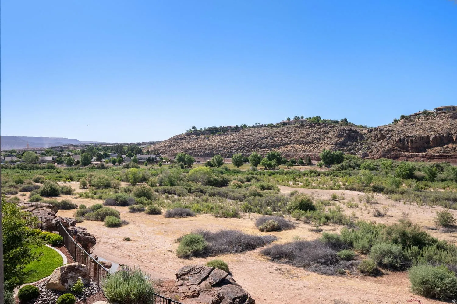 Expansive desert landscape featuring natural rock formations, distant residential structures, and vibrant green foliage