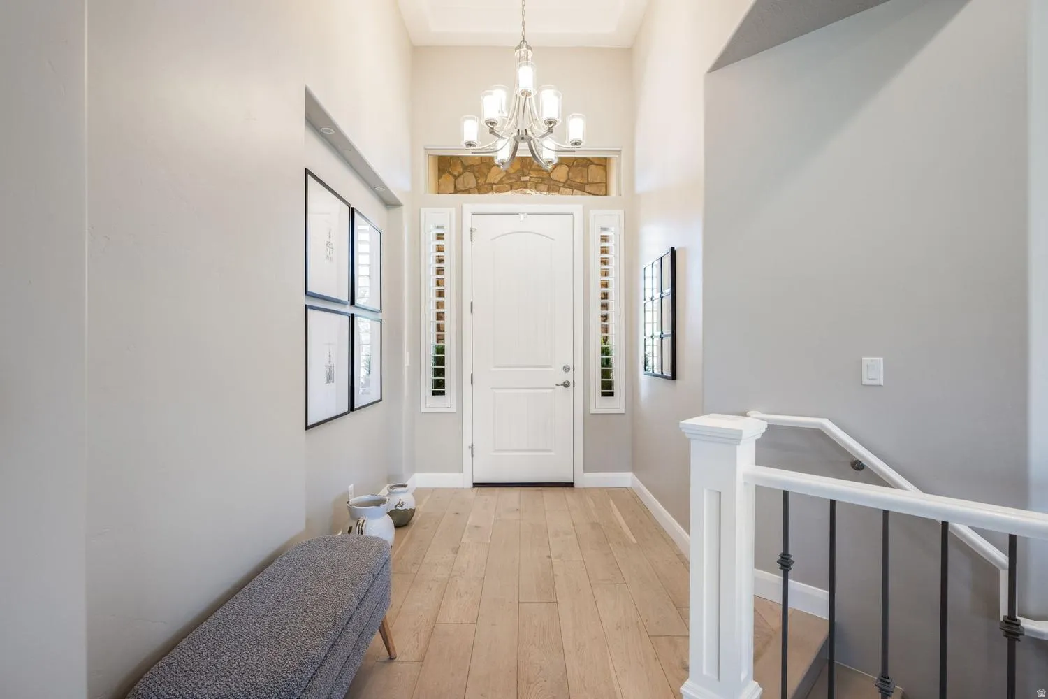 Two-story entryway featuring wood-finish flooring, a white paneled door with sidelights, and an overhead chandelier