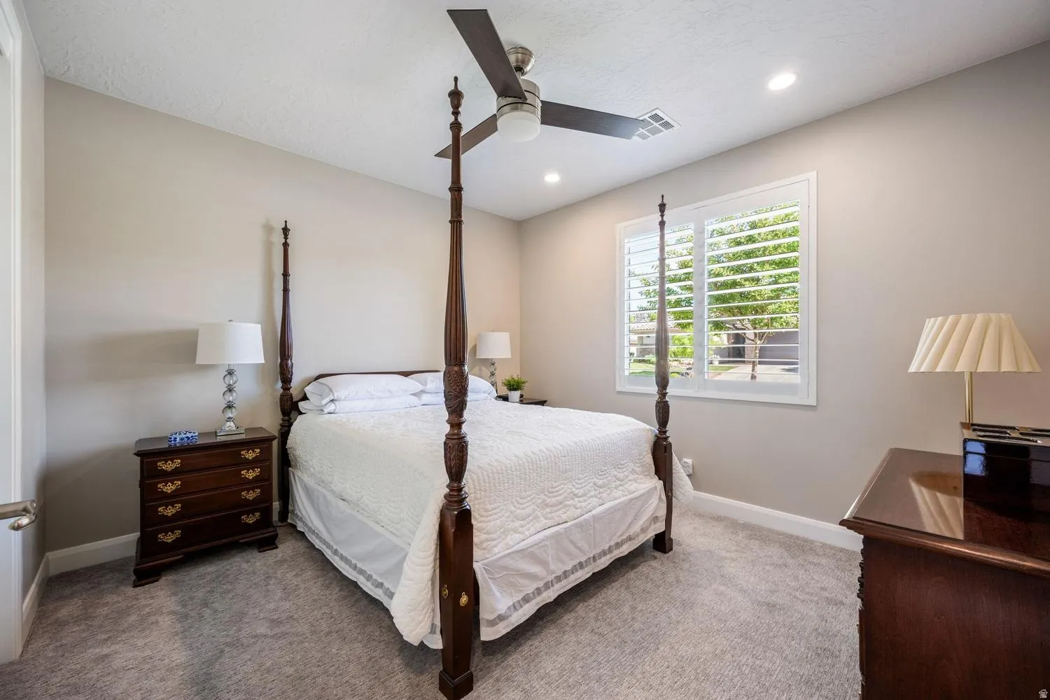 Neutral tone wall paint with recessed lighting, an overhead ceiling fan, white plantation shutters, and light grey carpet flooring