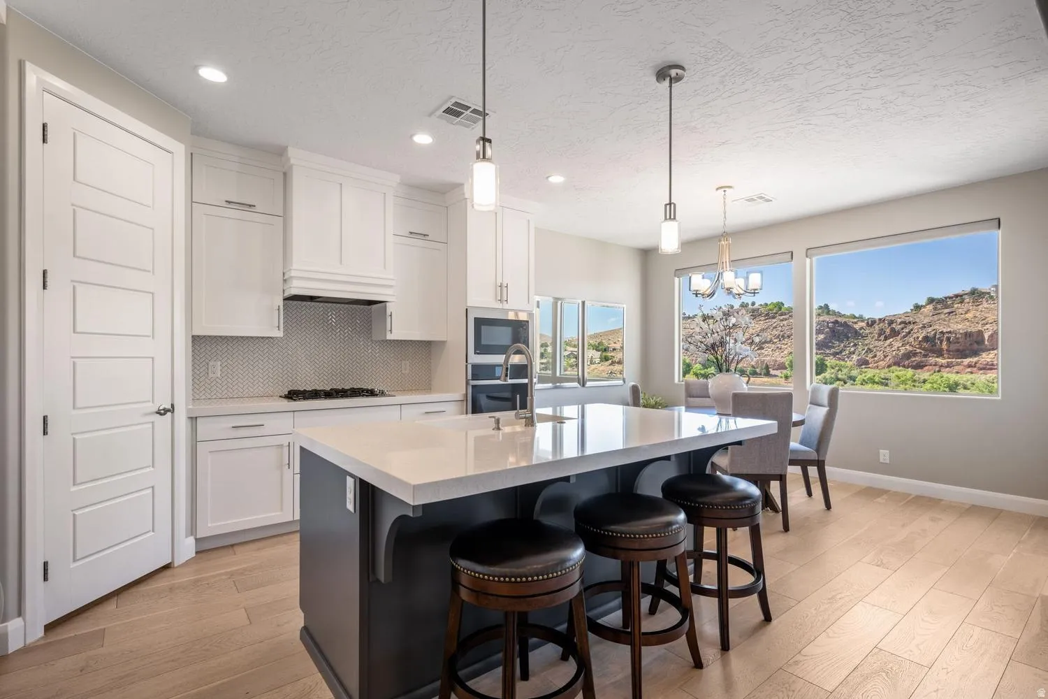 Kitchen featuring a large central island with a light-toned countertop, white cabinetry, a hexagonal tile backsplash, stainless steel appliances, and wood-finish flooring
