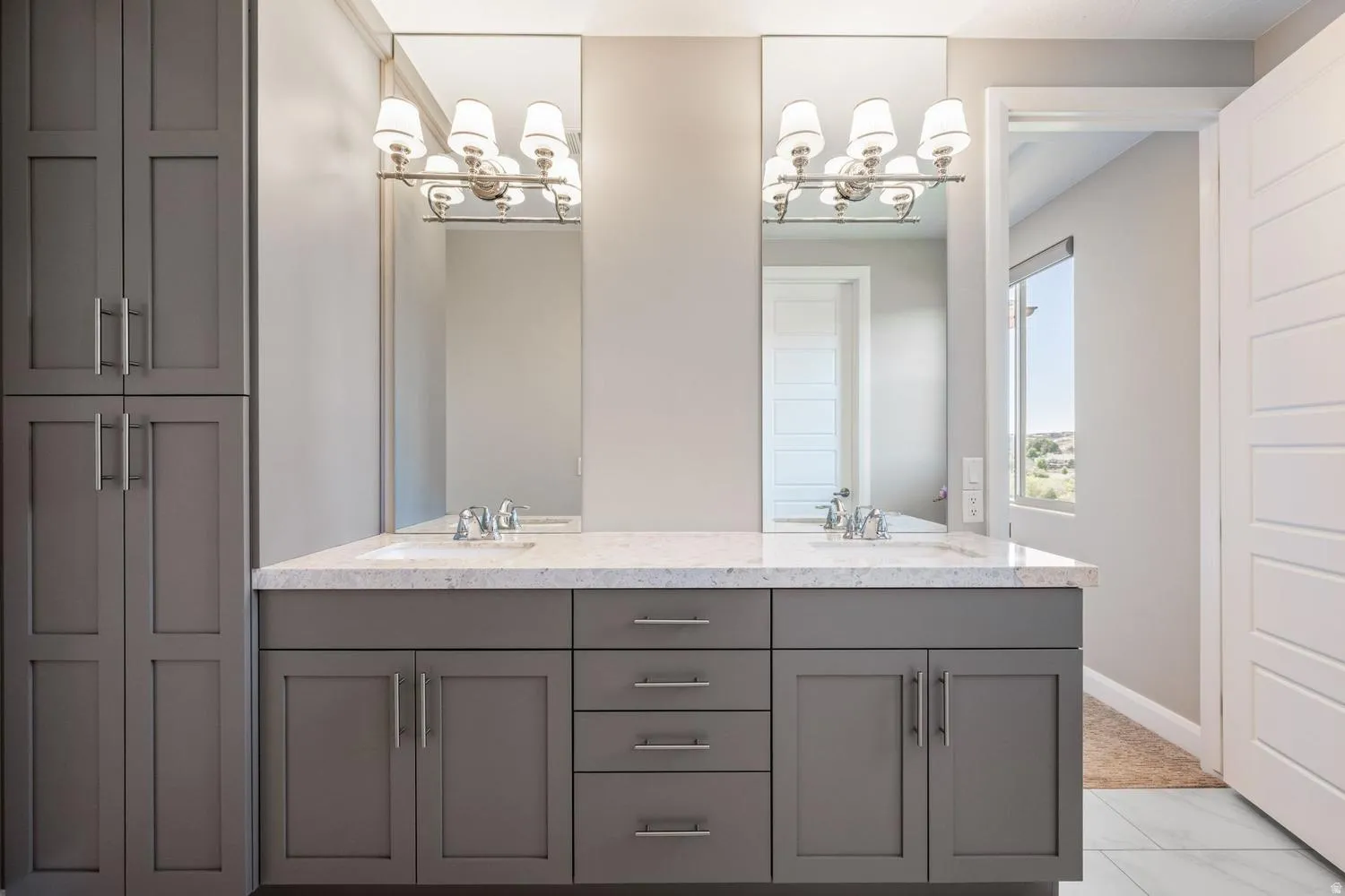 Dual vanity featuring gray shaker-style cabinetry, a light-toned countertop, two integrated sinks, and two mirrors with brushed nickel light fixtures